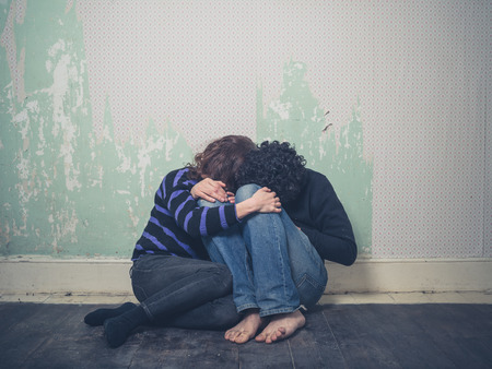 A sad young couple is sitting huddled up on  the floor in an empty roomの写真素材