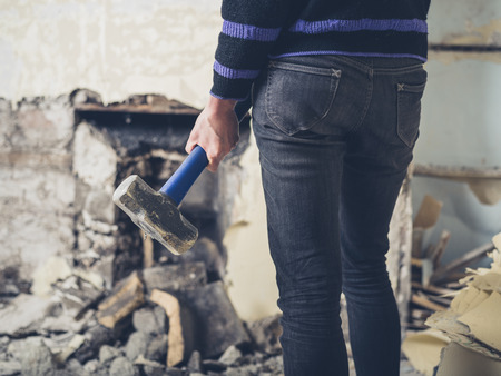 A young woman is opening up an old fireplace in a Victorian house with a sledge hammerの写真素材