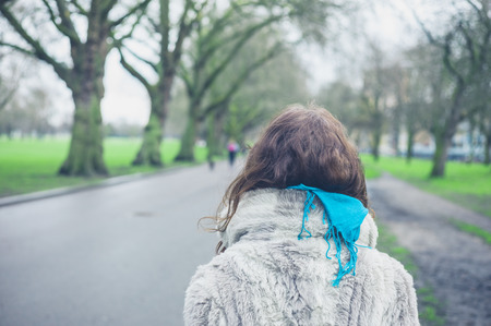 Rear view of a young woman in a fur coat walking in the park on a winter dayの写真素材