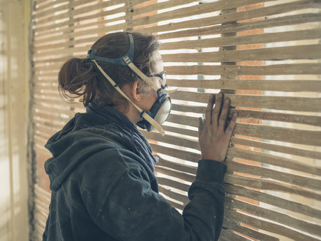 A young woman wearing protective workwear is peeping through an old wattle and daub wallの写真素材