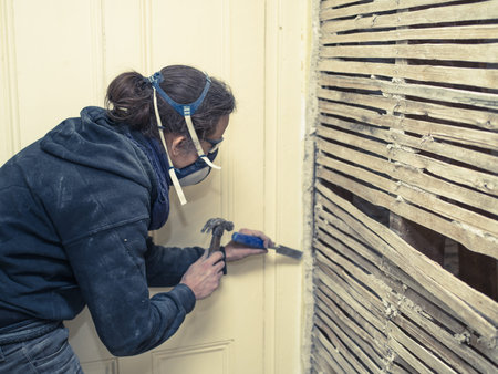 A young woman is repairing an old wattle and daub wall