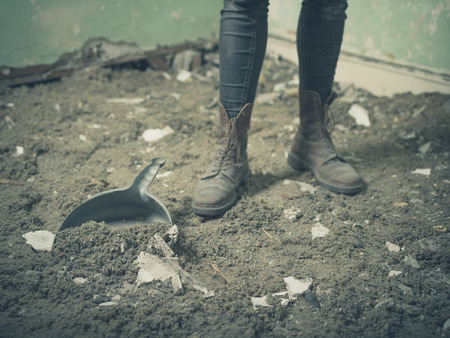 The feet of a person wearing boots by a dustpan on a floor covered with dirt and rubbleの写真素材