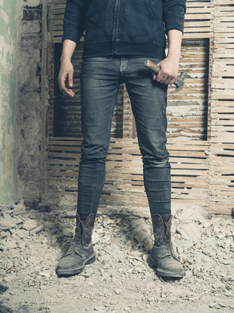A young woman holding a hammer is standing by an old wattle and daub wallの写真素材
