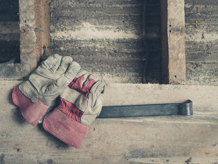 A pair of builders gloves and a crowbar on a wooden floor