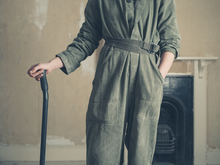 A young woman wearing a boiler suit is standing by a fireplace in a Victorian house with a crowbar in her handの写真素材