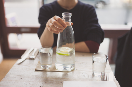 A young woman is sitting at a table in a restaurant and is drinking waterの写真素材