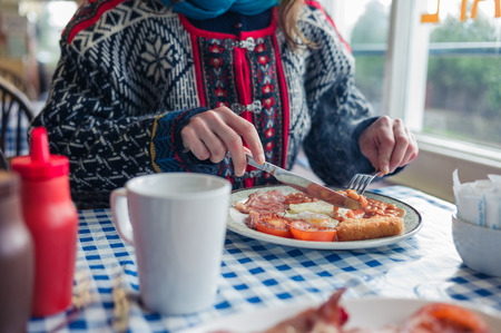 A young woman is having a traditional english breakfast with eggs, beans and baconの写真素材