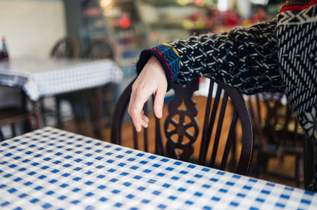 The hand and arm of a young woman resting on the back of a chair in a cafe