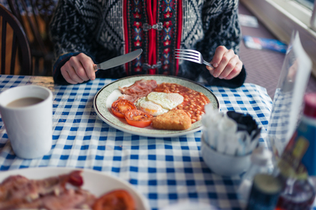 A young woman is having a traditional english breakfast with eggs, beans and baconの写真素材