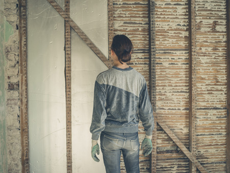 A young woman is standing in a loft room and is looking at the insulation she has put in the wallsの写真素材