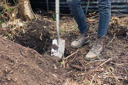 The feet of a person in boots standing by a hole with a spade