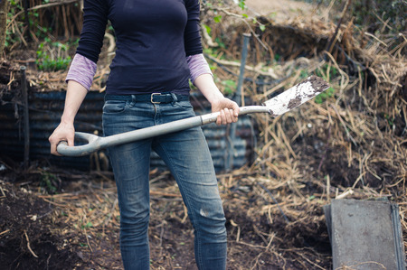 A young woman is standing in her garden with a spadeの写真素材