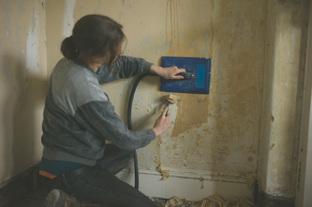 A young woman is removing wallpaper with a steamerの写真素材