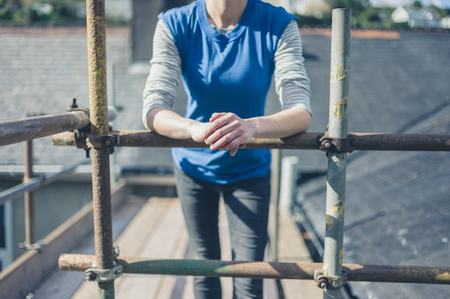 A young woman is standing on a scaffold by a roofの写真素材