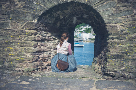 A young woman is relaxing under a stone arch by the sea