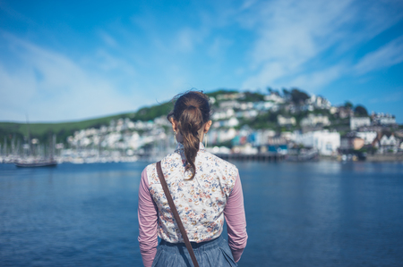 A young woman is standing by the water in a small village on a sunny summer dayの写真素材