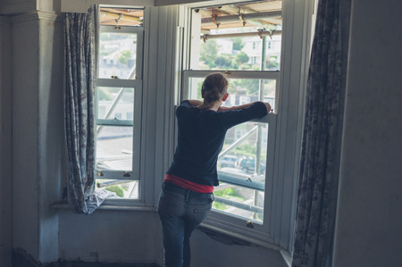 A young woman is standing by the window and looking at scaffolding outsideの写真素材
