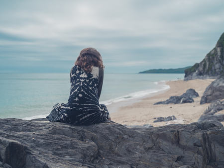 A young woman is sitting on some rocks by the seaの写真素材