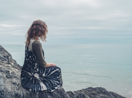 A young woman is sitting on some rocks by the sea