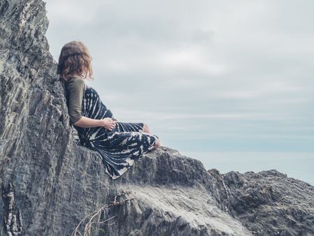 A young woman is sitting on some rocks by the seaの写真素材