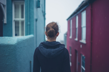 A young woman is standing by some houses in a small town on a foggy dayの写真素材