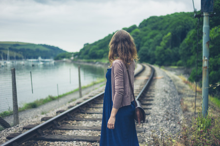 A young woman is walking near the railroad tracks by a riverの写真素材