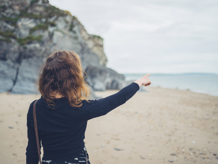 A young woman is standing on the beach and is pointing at the seaの写真素材