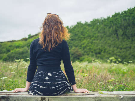 A young woman is sitting and resting on a bench in the countrysideの写真素材