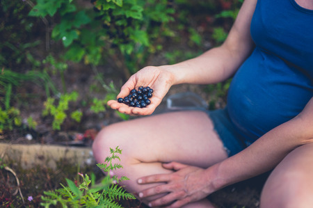 A young pregnant woman is sitting in her garden by a black currant bushの写真素材