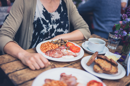 A young woman is having a traditional english breakfast in a cafeの写真素材