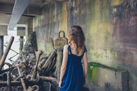 A young woman wearing a dress is exploring a shipyard with rusty old anchorsの写真素材