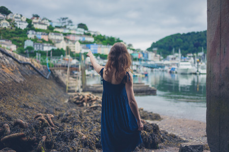 A young woman is standing in a desolate shipyard and is pointing at a small townの写真素材
