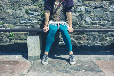 A young woman is sitting on a bench outsideの写真素材