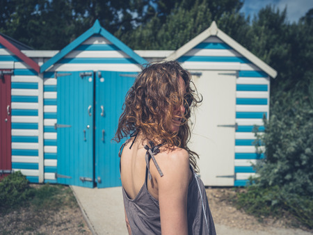 A young woman with wind swept hair is standing by some beach hutsの写真素材