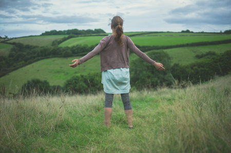 A young woman is in the countryside expressing freedom and joy with her armsの写真素材
