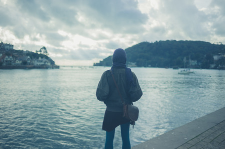 A young woman is standing by a river in a small townの写真素材