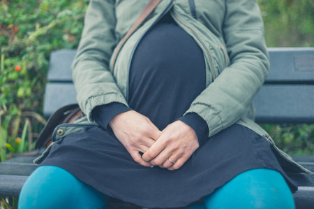 A young pregnant woman is sitting on a bench outside