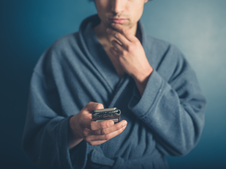 A young man wearing a bathrobe is using his smart phoneの写真素材