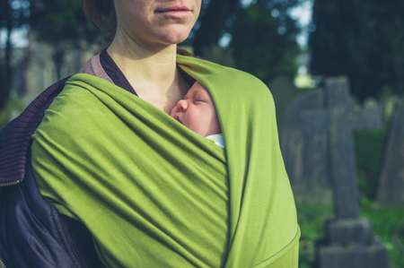 A young mother is standing in a cemetary with her baby in a slingの写真素材