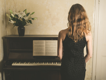 A beautiful young woman in a dress is standing by a pianoの写真素材