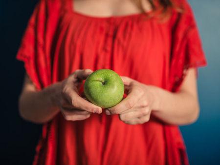 A young woman in a red dress is holding an appleの写真素材