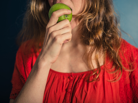 A young woman in a red dress is eating an appleの写真素材