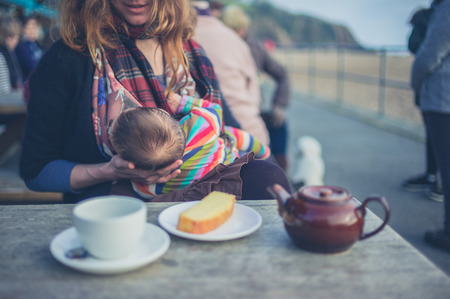 A young mother is breastfeeding her baby in a cafe outside by the beach in winterの写真素材