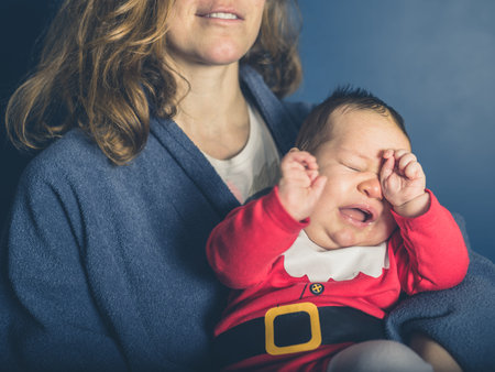 A mother is holding a sad little baby wearing a santa costume