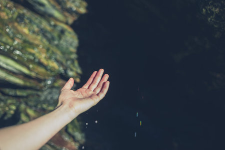 The hand of a young woman is catching some water drops in a cave