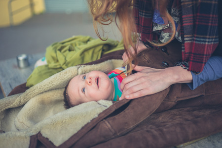 A young mother is wrapping her baby in a coat outsideの写真素材