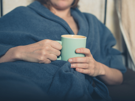 A young woman wearing a bathrobe is drinking a cup of tea in bedの写真素材