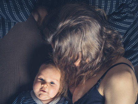 A cute little baby on a bed with his motherの写真素材