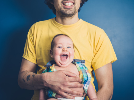 A young father is posing with his happy baby on a blue backgroundの写真素材