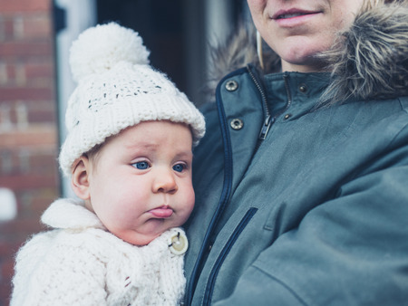 A young mother and baby in winter clothes outside the houseの写真素材
